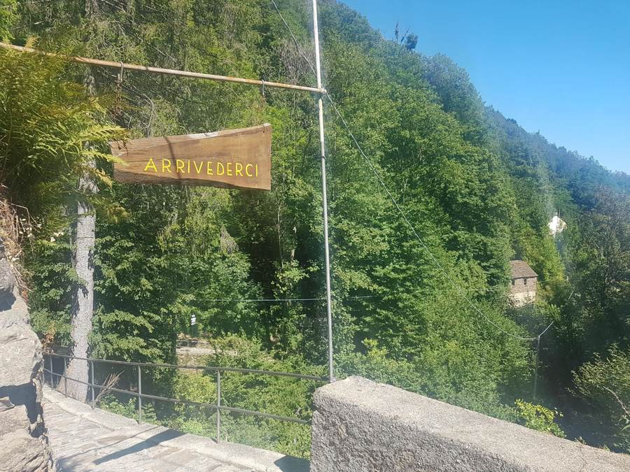Gravel track along a stone wall above the Cannobino Valley, with a hanging sign