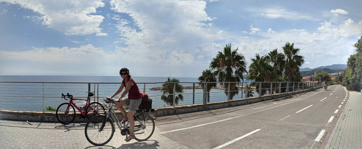 Two cyclists riding a palm-lined coastal road near Cipressa, Liguria