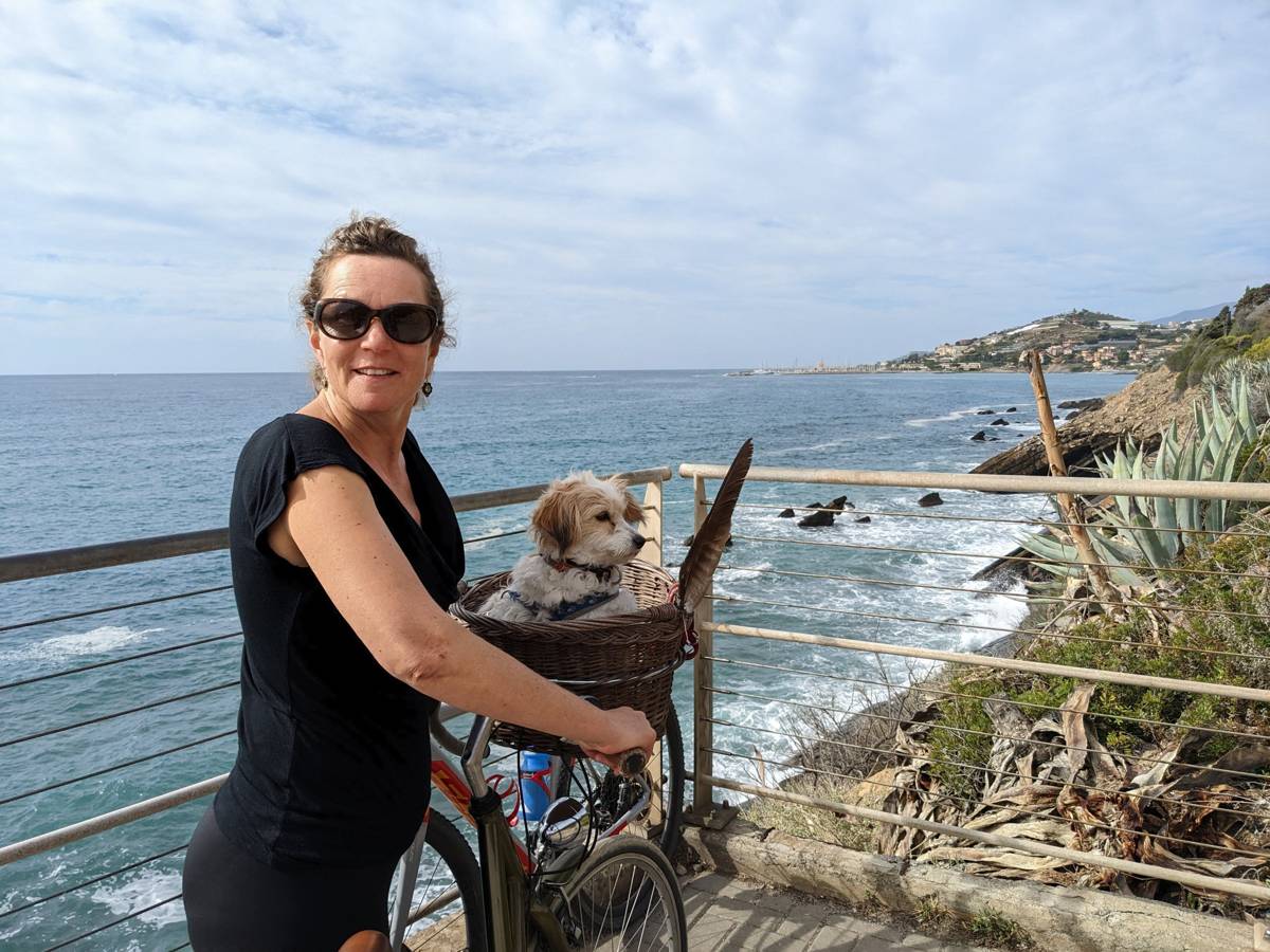 Kevin's wife with their dog Lillie in a bike basket at a coastal viewpoint near Cipressa