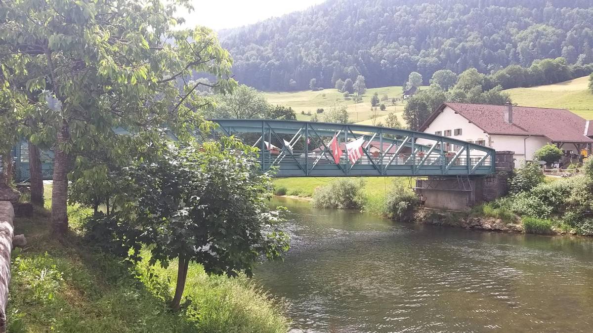 A green truss bridge crossing the Doubs river near Goumois village