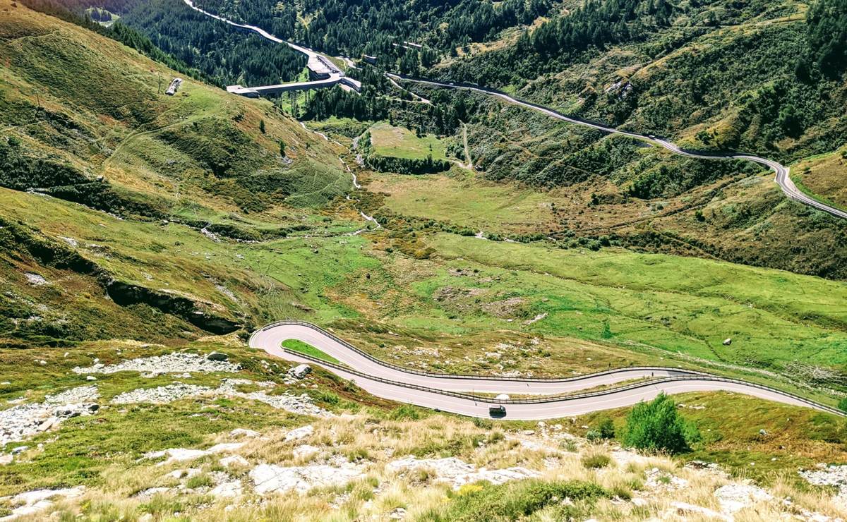 A switchback mountain road climbing through a green valley near Bionaz, Aosta Valley