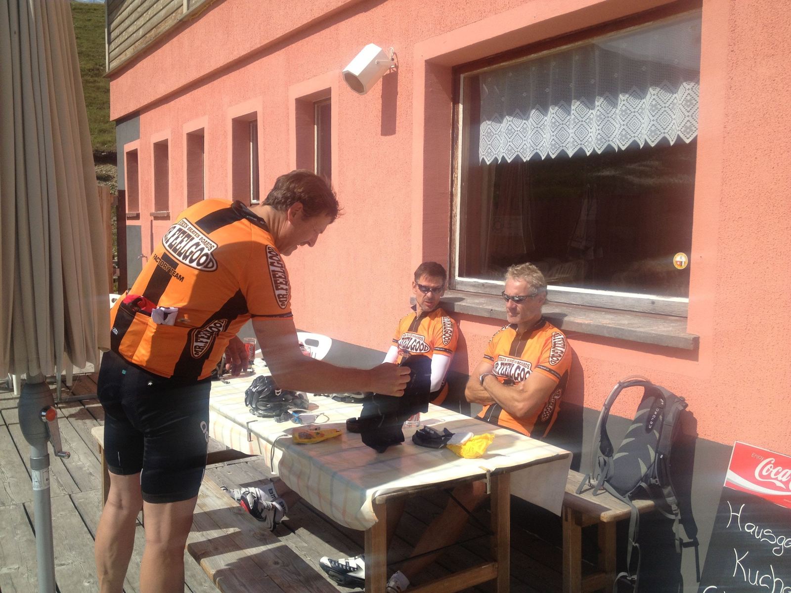 Kevin and two riding companions in orange Mr Feelgood team jerseys at a cafe table after the ride