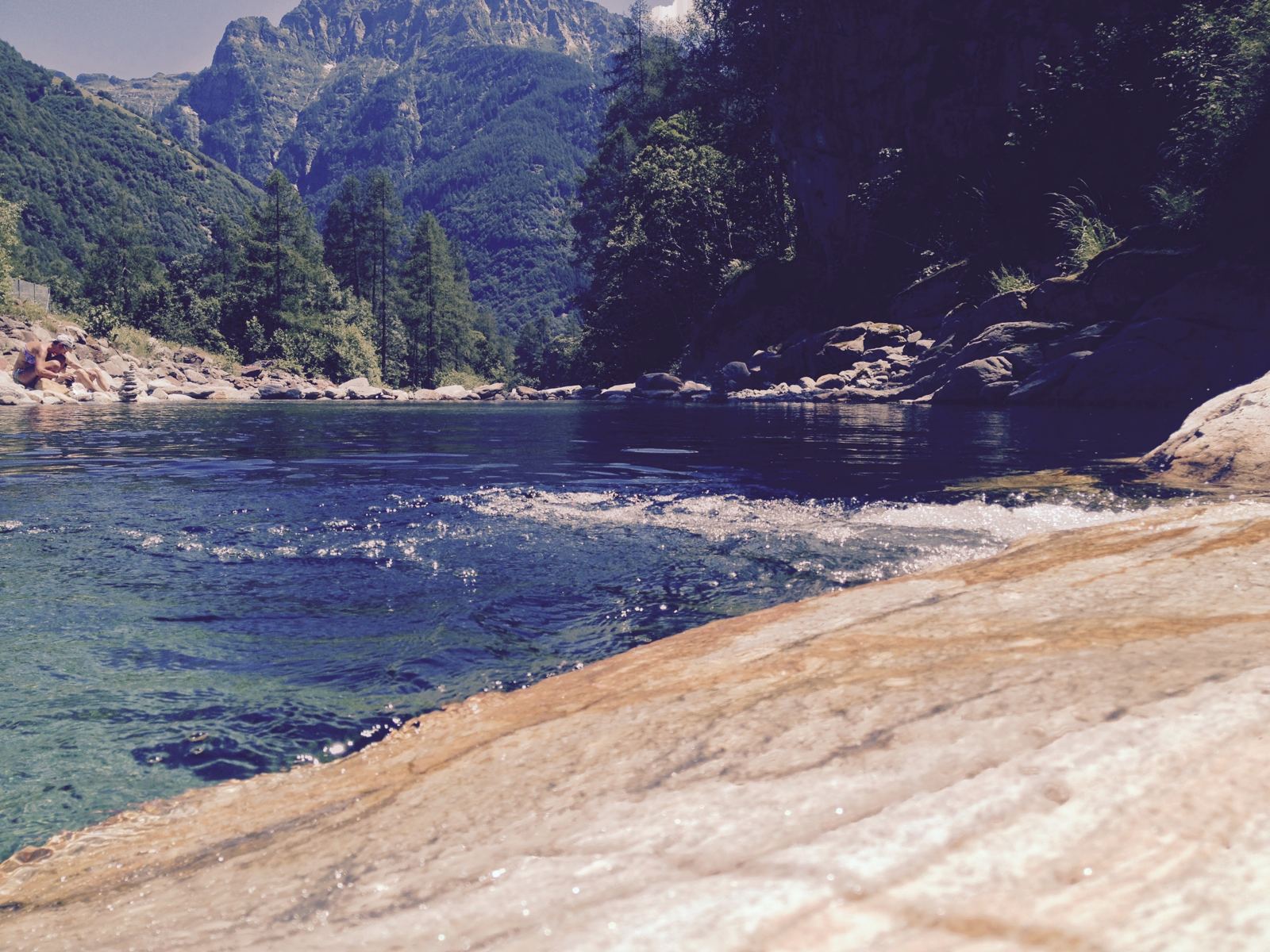 A swimming spot in the emerald Verzasca river near Sonogno, with mountains behind