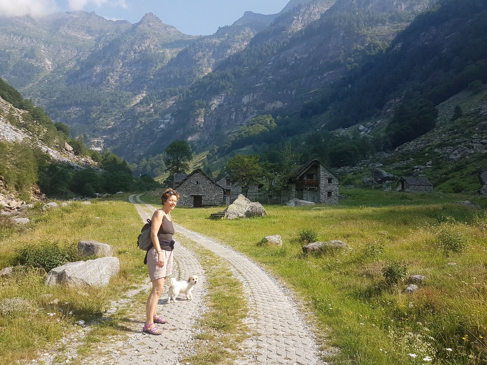 Kevin's wife and their dog Lillie walking a gravel track toward a stone hamlet in the Verzasca Valley
