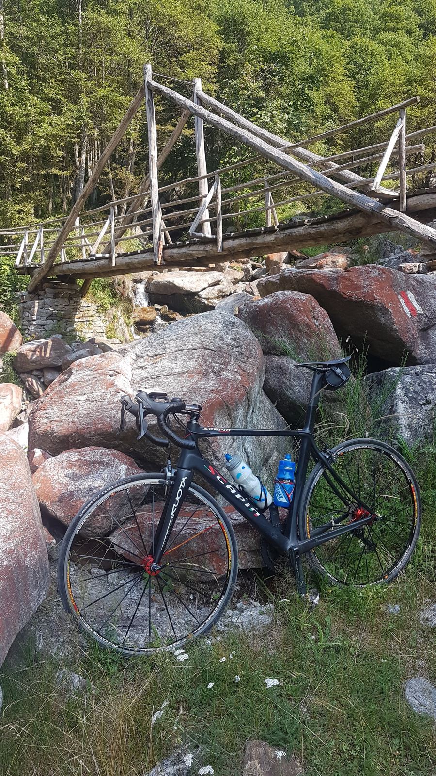 A road bike leaning against red rocks beside a suspension bridge in the Verzasca Valley